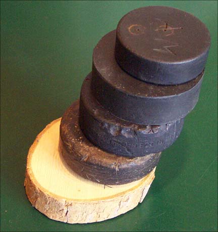 Top - Child's Rubber Puck c.1940s, Vulcanized Rubber Puck c.1930, Well Used Rubber Puck c.1920, Multi-Layered Leather Puck c.1915, Bottom - Wooden Puck 